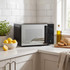 Black microwave oven on kitchen counter with lemons, olive oil, and sliced bread nearby
