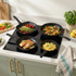 Set of four black non-stick frying pans on induction hob, each cooking different food.