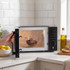 Black microwave oven on kitchen counter with bowl of chocolate inside, door being opened