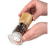 Manual pepper mill with clear body and wooden top, held in both hands and filled with peppercorns