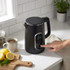 Black electric kettle with digital display, shown on kitchen worktop in use