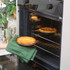 Golden pie in black baking dish, being placed in oven, kitchen background visible