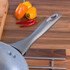 Grey non-stick frying pan handle close-up on wood worktop with peppers and chillies.