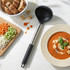 Black and silver soup ladle beside bowl of tomato soup and chopped vegetables