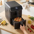 Black digital air fryer with chicken skewers cooking in basket on wooden kitchen counter