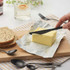 Black butter knife spreading butter onto open block beside seeded bread slice