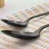 Set of two black stainless steel spoons on white cloth with yellow spots