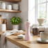 Light pink salt mill on kitchen worktop near bowl of salt, coffee jar, and cup