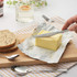 Stainless steel butter knife spreading butter on a wooden board with seeded bread slices