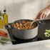 Grey cooking pot with handles, filled with vegetable stew on hob, hand stirring
