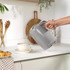Grey electric kettle pouring hot water into a teacup on a kitchen counter