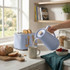 Blue kettle pouring hot water into mug beside matching toaster in kitchen setting
