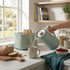 Sage green kettle pouring water beside matching toaster, breakfast setting