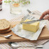Silver butter knife spreading butter on board with seeded bread slices and spoons