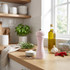 Pink salt grinder on kitchen counter with fresh herbs and oil bottle nearby