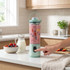 Portable mint green blender making berry smoothie in modern kitchen