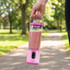 Pink portable blender with smoothie inside, held by handle outdoors