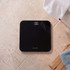 Black digital bathroom scale with LED display, shown on tiled floor.