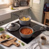 Grey saucepan with black handle cooking vegetable soup on hob, hand stirring with wooden spoon