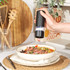 Hand using black electric salt grinder above bowl of steak salad on kitchen worktop.