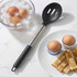 Slotted black and silver serving spoon next to soft boiled eggs and toast on white counter