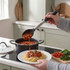 Serving tomato sauce onto spaghetti using a black and silver kitchen spoon