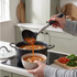 Black and silver ladle serving vegetable soup from pot to bowl in kitchen