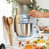 Blue stand mixer with stainless steel bowl on kitchen counter, hand adding egg.