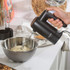 Black electric hand mixer with dough hook mixing dough in a silver bowl on kitchen worktop