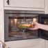 Hand placing dish with salmon and vegetables in built-in microwave oven