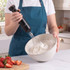 Person using black handheld electric whisk to whip cream in ceramic bowl, kitchen background