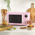 Pink microwave oven with digital display, shown on a kitchen counter with cooked food