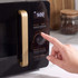 Black microwave with gold handle and controls, close-up of dial being adjusted