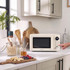 Cream microwave on kitchen counter with breakfast ingredients and hand pressing control dial