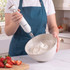 White hand blender with whisk attachment whipping cream in a bowl, kitchen setting