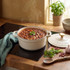 Cream cast iron casserole pot with stew, steam rising, on hob with lid and ingredients nearby