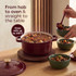 Red cast iron casserole dish with lid on rustic kitchen table, surrounded by fresh ingredients