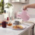Pink electric kettle pouring hot water into a mug on a kitchen counter