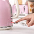Close-up of hand switching on pink electric kettle, highlighting power lever feature.