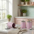 Set of three pink kitchen canisters for sugar, tea, and coffee on a countertop.