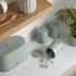 Set of three sage green kitchen storage canisters and bread bin, tea bags shown.