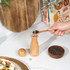 Wooden pepper mill being filled with black peppercorns in a kitchen setting