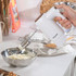 White hand mixer with wood effect accents mixing cream in a stainless steel bowl