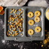 Grey non-stick baking tray with two sections, filled with mixed nuts and round biscuits.