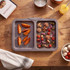 Person removing tray of roasted potatoes and vegetables from oven in home kitchen.
