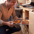 Non-stick grey baking tray with roasted vegetables on kitchen worktop, family cooking in background