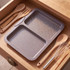 Grey two-section oven tray in wooden kitchen drawer with utensils