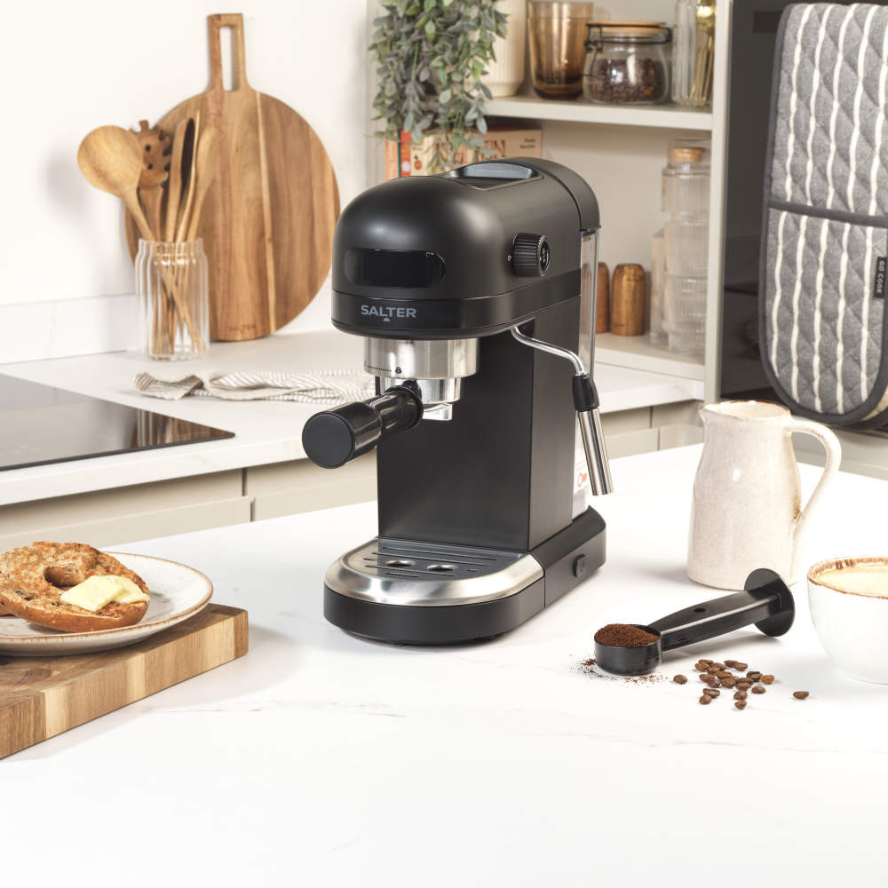 Black espresso machine on kitchen counter with coffee scoop and mug