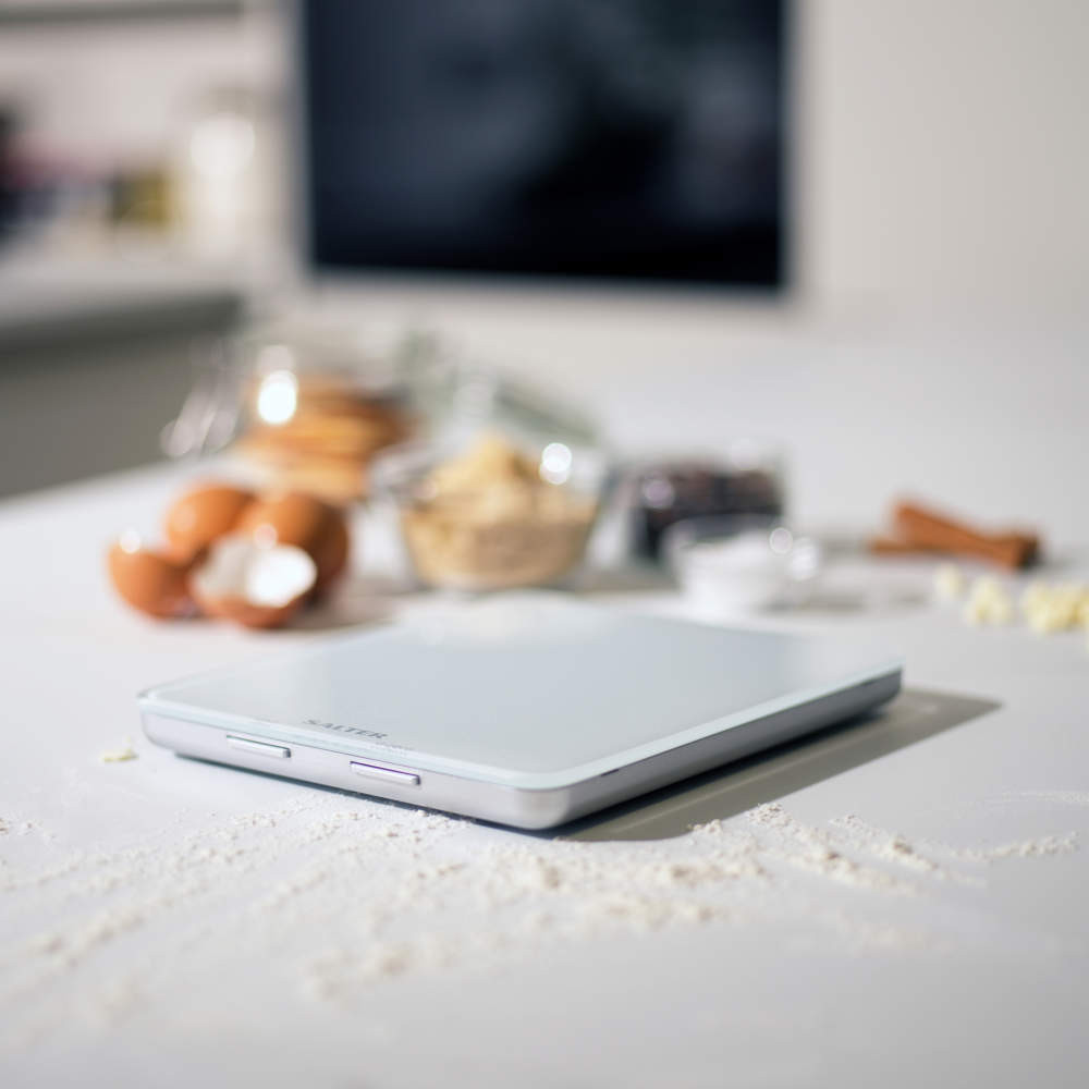 White digital kitchen scale on worktop with baking ingredients in background