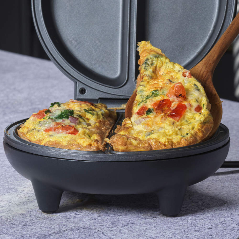 Electric omelette maker with cooked vegetable omelette inside, one slice being served